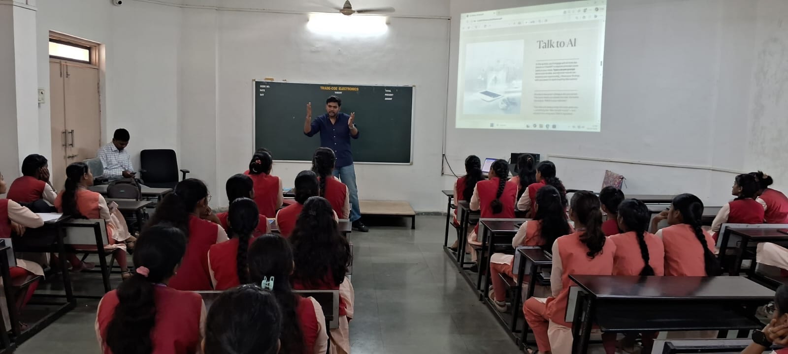 Facilitator leading an AI literacy session with students in a classroom, a presentation slide reading 'Talk to AI' displayed on screen.