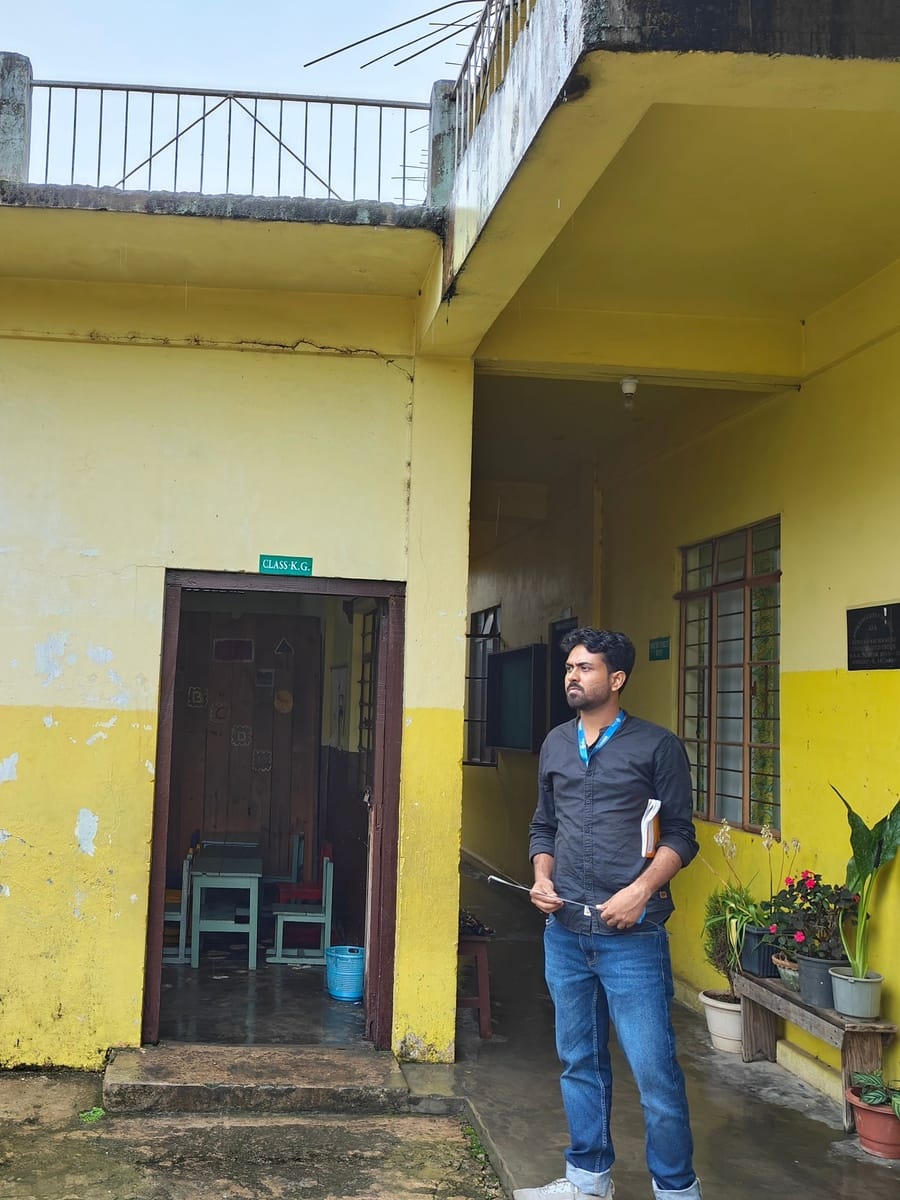 A field team member standing beside an open classroom door at Seng Khasi School, Mawlai, Meghalaya