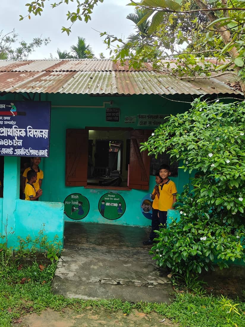 Students in yellow uniforms at the window and door of a classroom at Nowchaliyan Gaon LP School, Jorhat, Assam