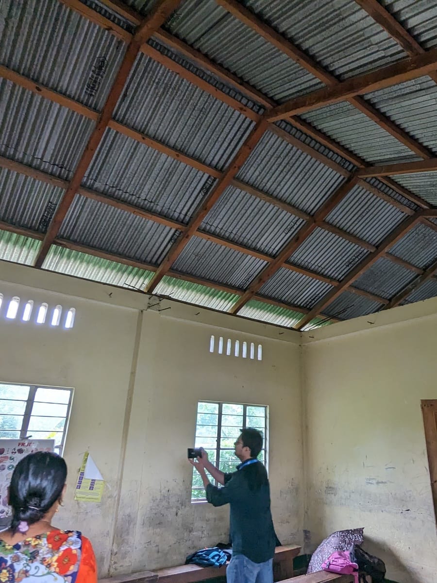 A field team member photographing an empty classroom while a teacher looks on at Seng Khasi School, Ri-Bhoi District, Meghalaya