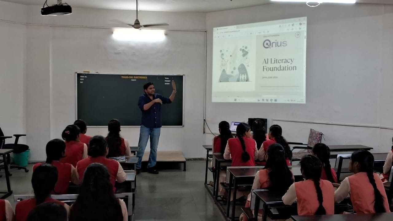 A facilitator gesturing at the front of an ITI classroom, with a QriusAI Literacy Foundation slide projected beside the blackboard