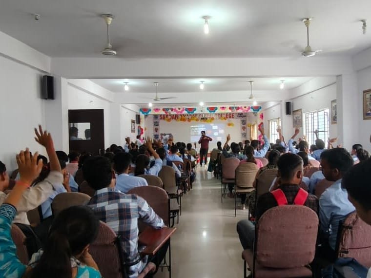 Students raising their hands across a long college hall while a facilitator stands at the screen