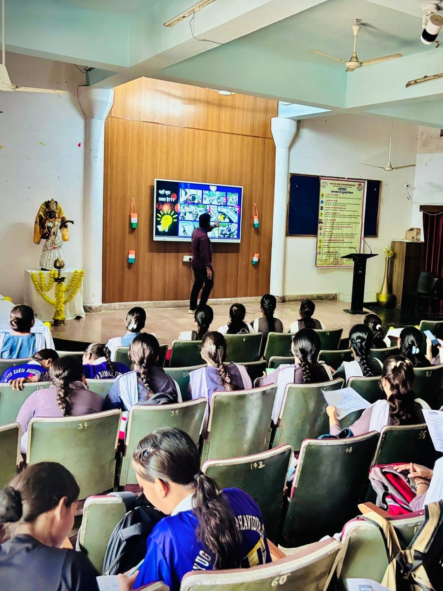 A facilitator pointing at a screen at the front of an auditorium full of students at Navyug Kanya Mahavidyalaya, Lucknow