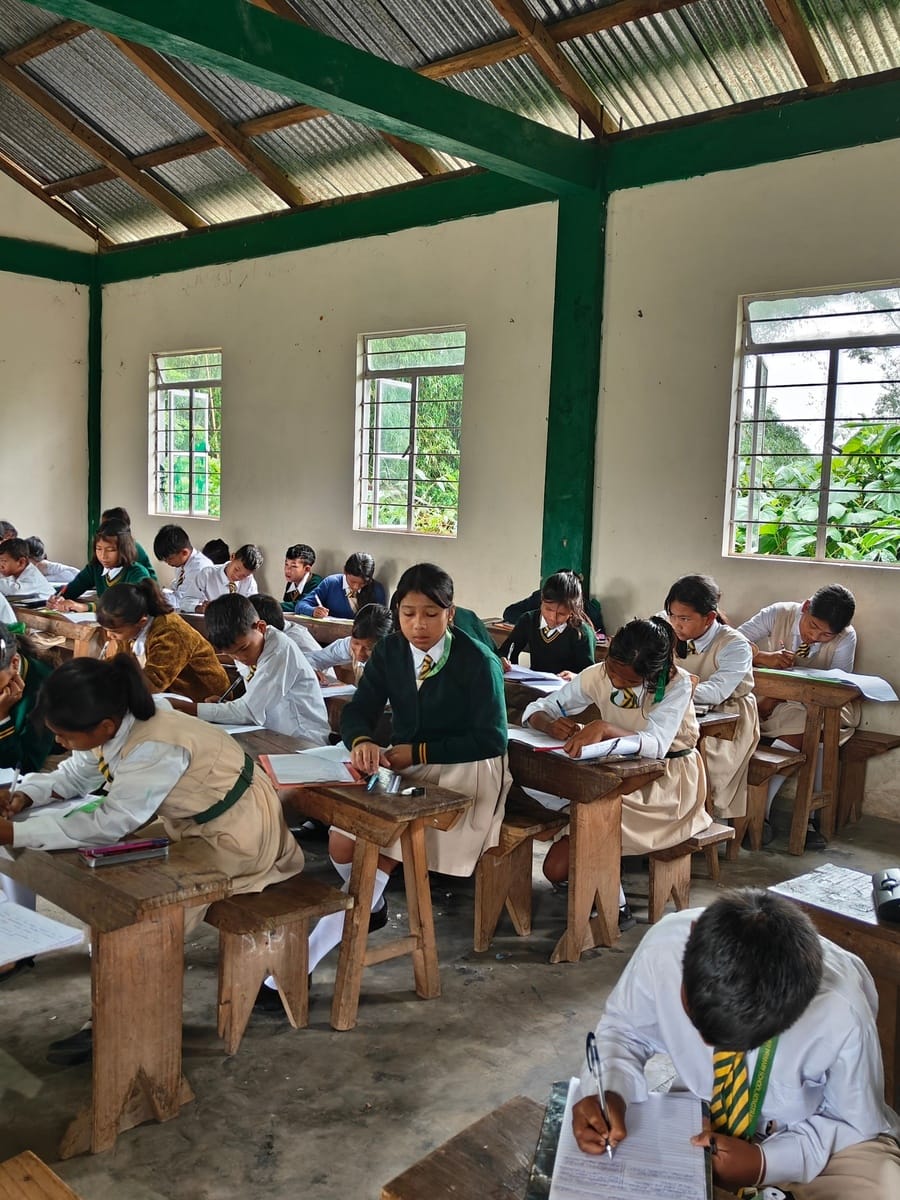Students in school uniforms writing at wooden desks in a classroom at Seng Khasi School, Ri-Bhoi District, Meghalaya