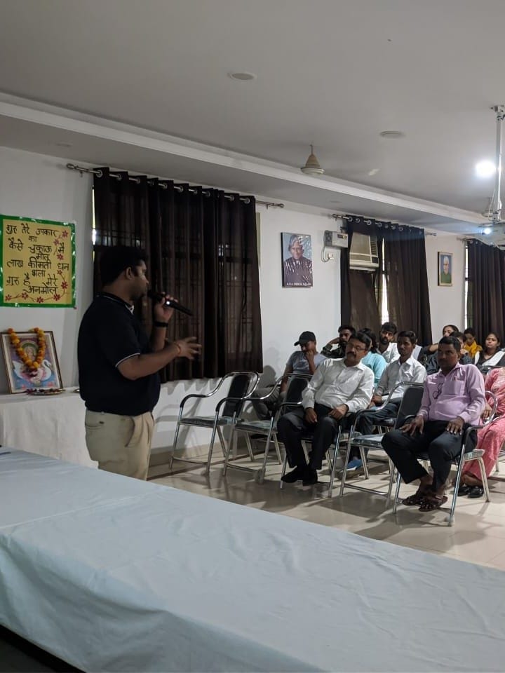 A facilitator with a microphone speaking to seated teachers and students in a hall